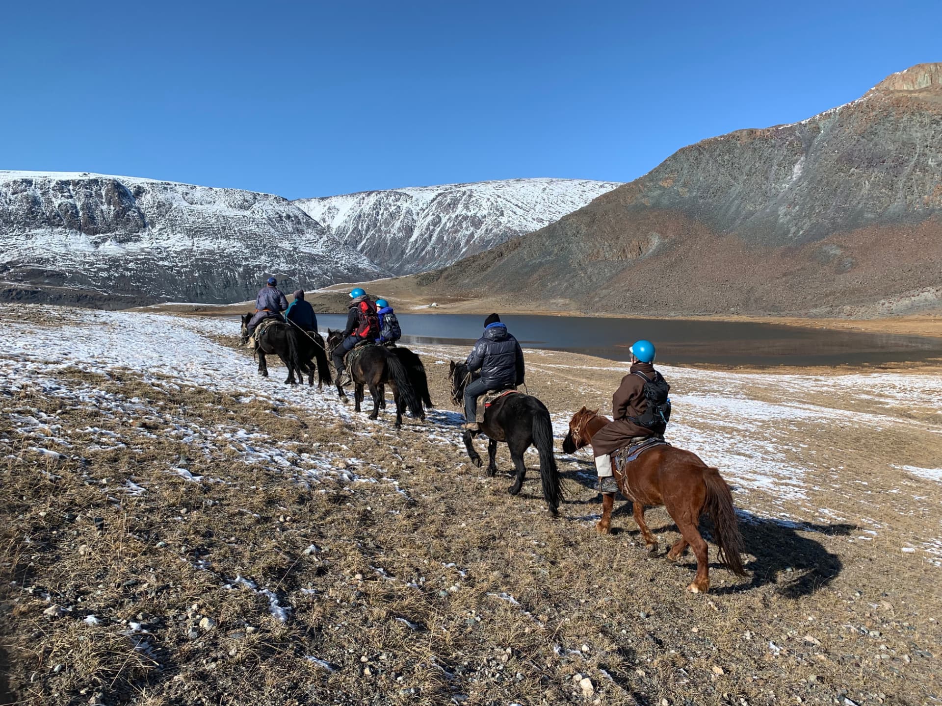 Riders horse trekking beside an alpine lake in the Altai Tavan Bogd