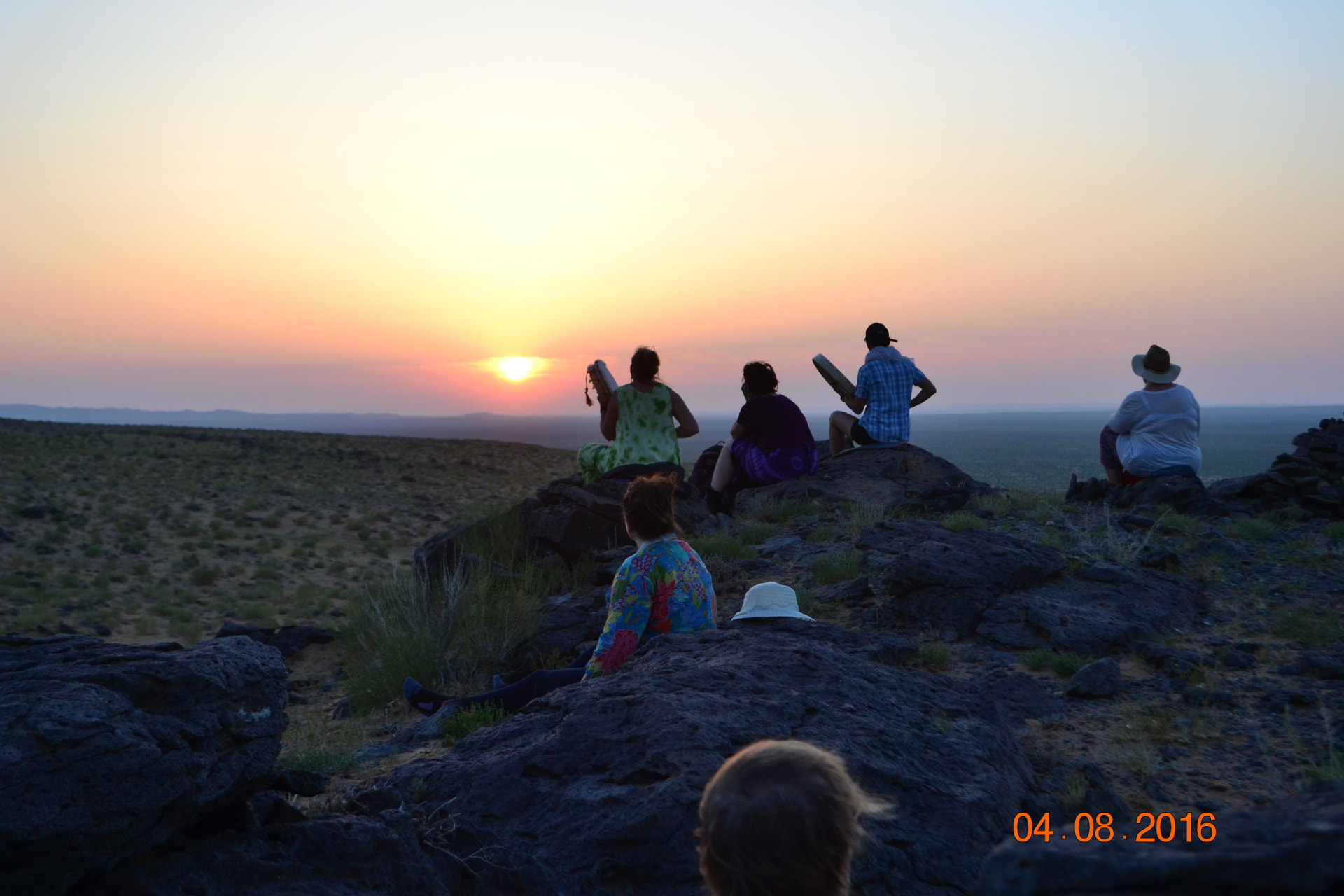 Travellers drumming together on a rocky ridge at sunset in the Gobi