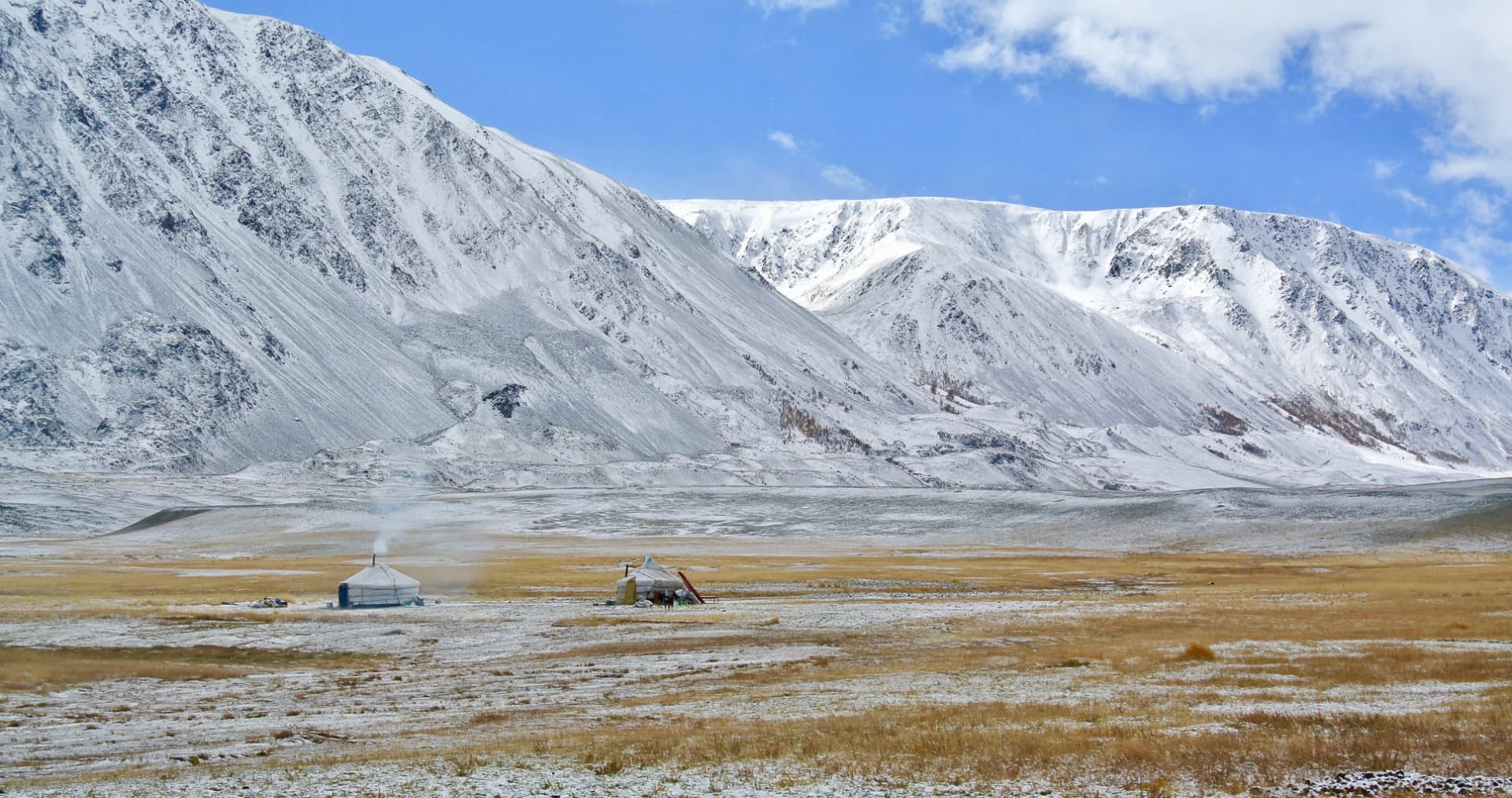Two gers with smoke rising below the snow-covered Altai Tavan Bogd