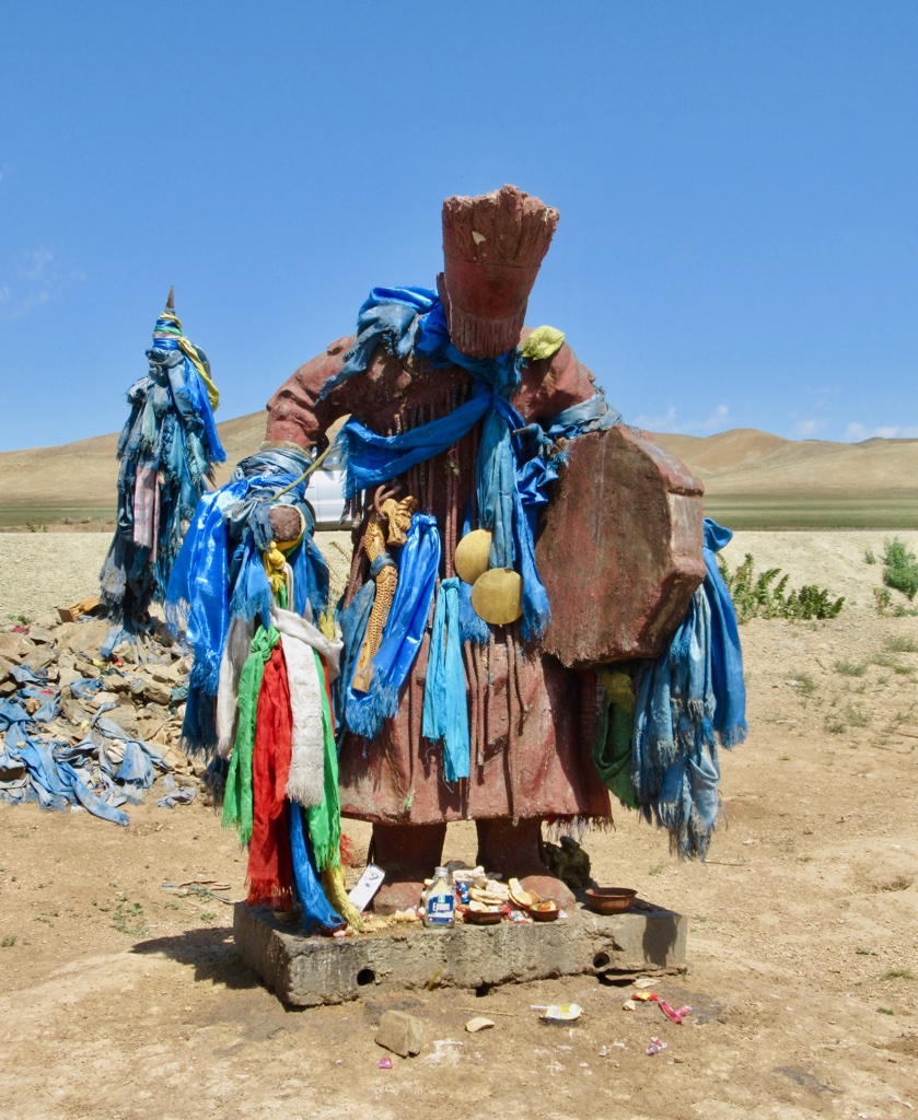 Shaman statue with offerings and blue prayer scarves
