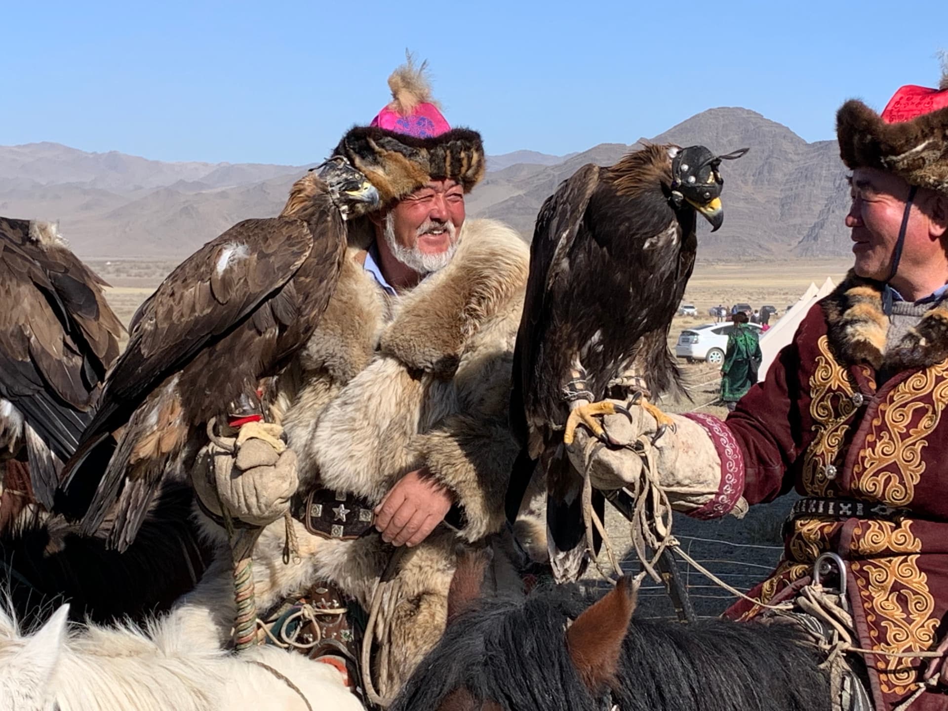 Two Kazakh eagle hunters laughing together, golden eagles perched on their gloves