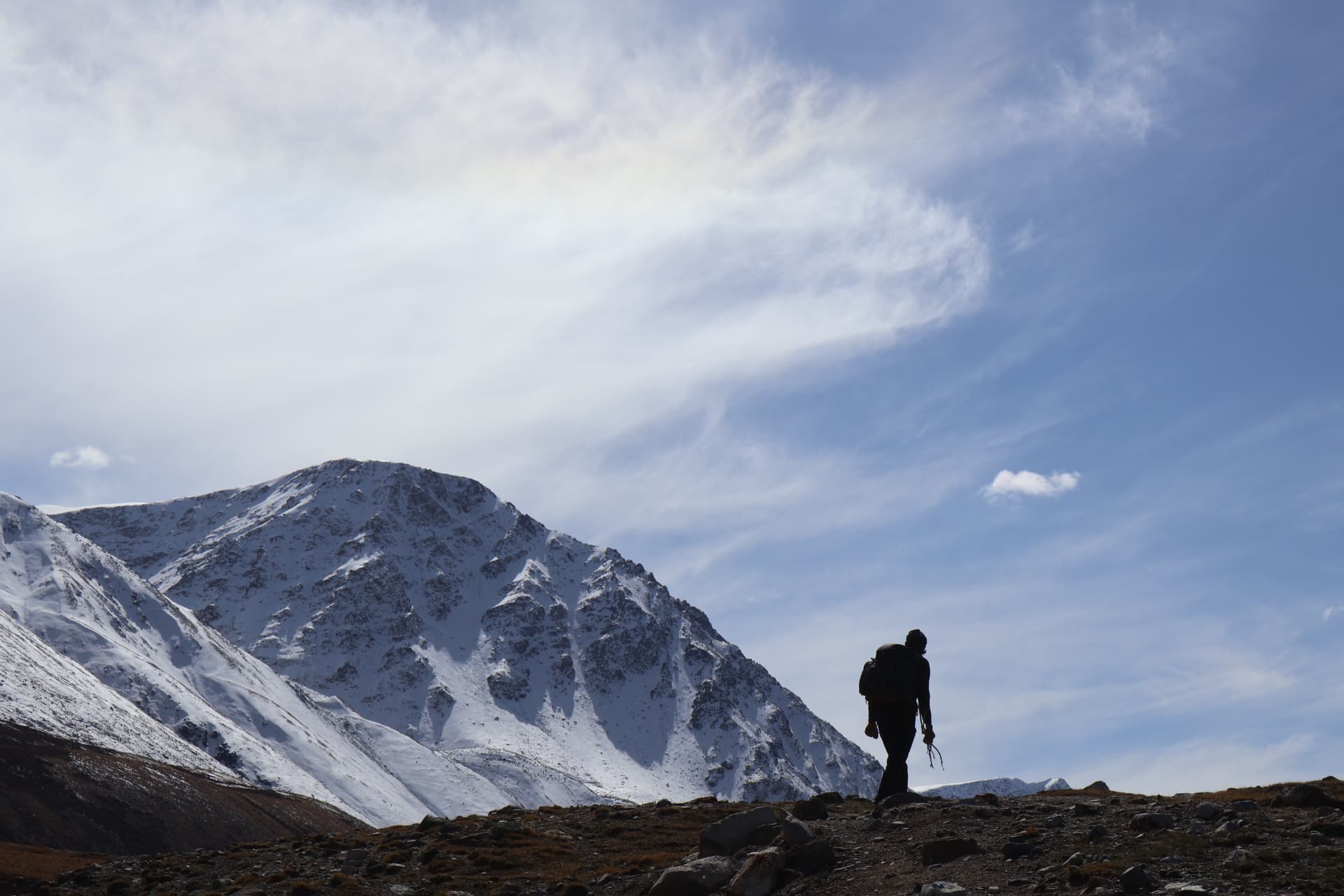 Silhouetted hiker walking a rocky ridge beneath snow-capped Altai mountains