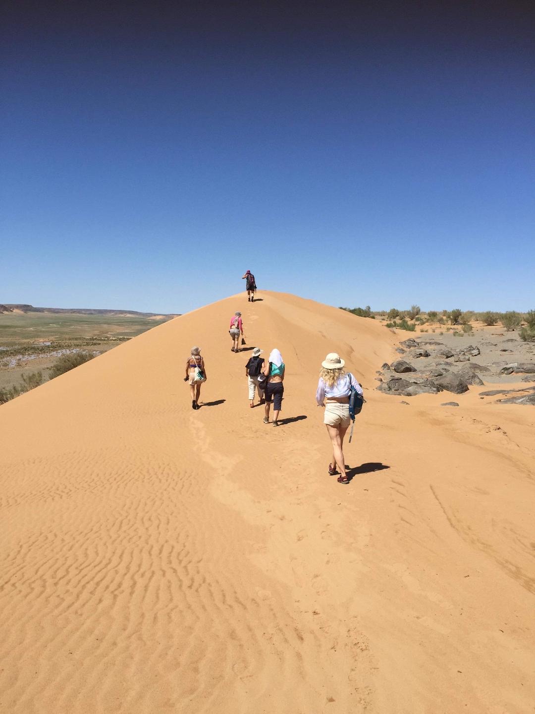 Retreat group walking up a red sand dune in the Gobi desert
